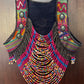A colorful beaded vest with a dark navy blue fabric base, featuring intricate multicolor beadwork, fringe details, and decorative metal buttons, displayed against a dark wood background.