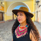 Woman wearing a brown hat and colorful necklace in front of a the famous santa catalina yellow arch in Antigua Guatemala