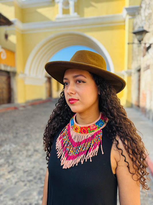 Woman wearing a brown hat and colorful necklace in front of a the famous santa catalina yellow arch in Antigua Guatemala