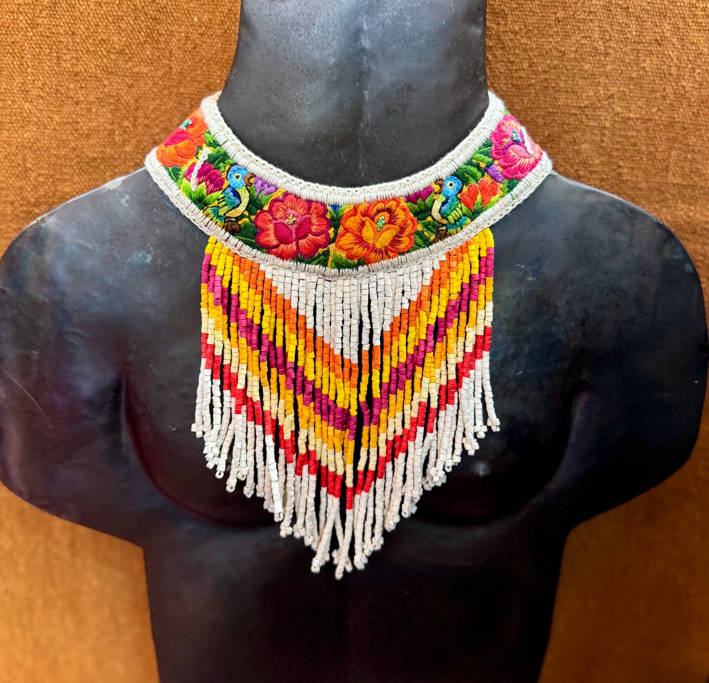 Colorful beaded necklace on a mannequin bust against a brown background